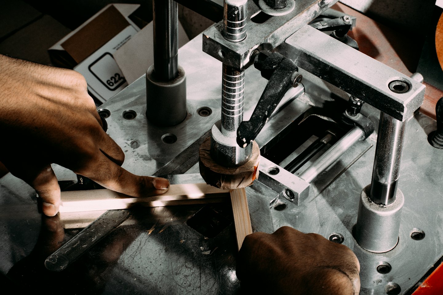 Hands operating a framing machine to join wood strips.